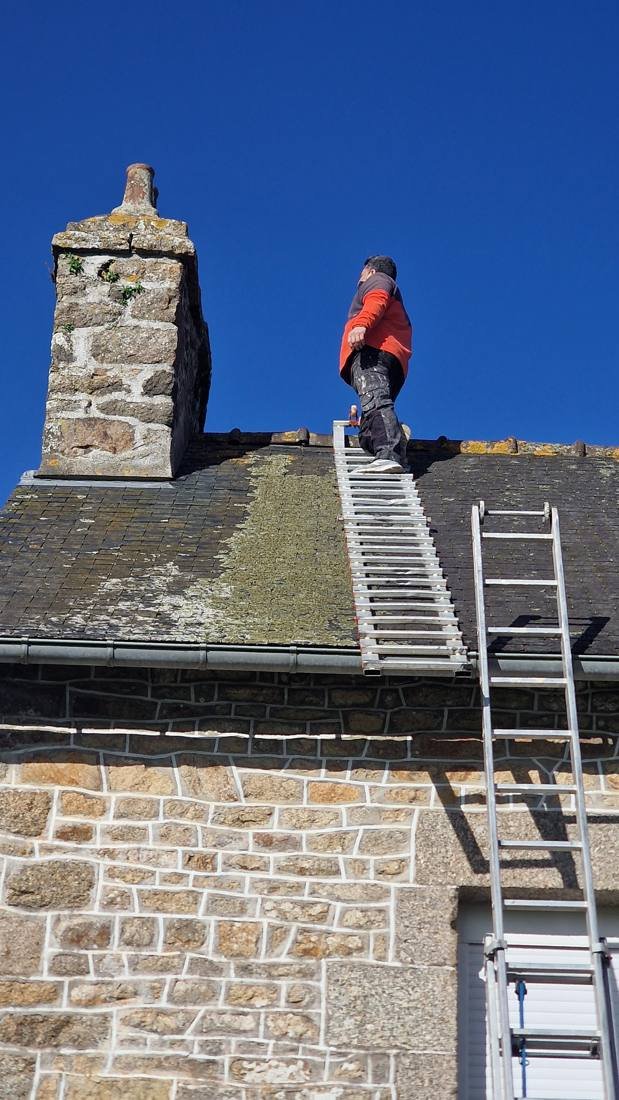 Artisan au sommet d'une échelle de toit près d'une cheminée en pierre