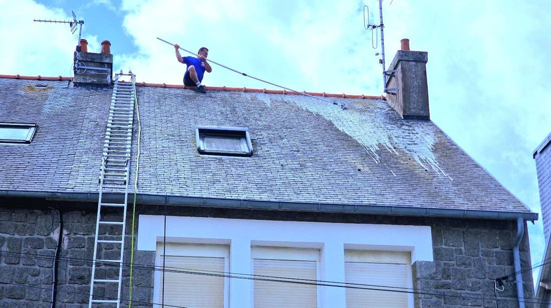 Artisan sur le faîtage d'un toit en ardoise avec une perche de traitement