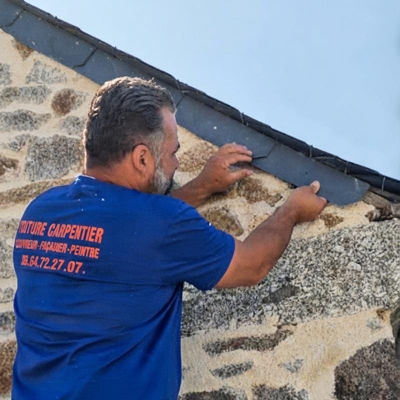 Artisan Toiture Carpentier posant une ardoise en rive d’un pignon en pierre