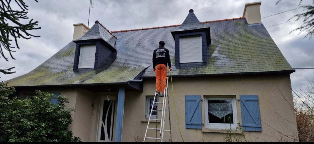 Couvreur sur une échelle devant une toiture en ardoise couverte de mousse