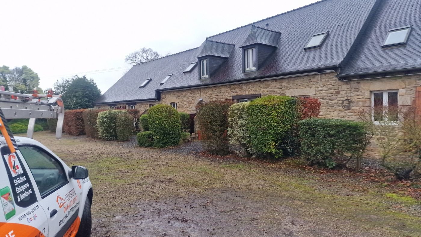 Longère en pierre à toiture d’ardoise avec lucarnes à Matignon, véhicule Toiture Carpentier au premier plan