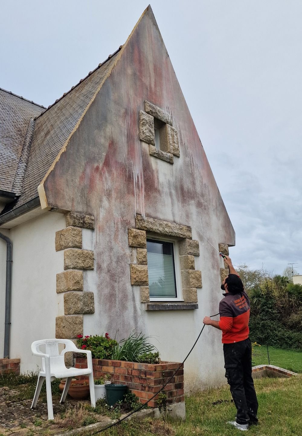 Artisan nettoyant à l’eau le pignon d’une maison dont la façade est tachée d’algues rouges, à Binic-Étables-sur-Mer